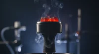 Крупный план раскалённых углей в калауде на чаше кальяна, с акцентом на жар и лёгкий дым.