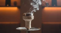 Крупный план кальянной чаши с устройством управления жаром, из которой поднимается легкий дым, на фоне размытого интерье