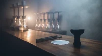 Рабочее место кальянного мастера с инструментами для забивки: щипцы, фольга, чаша, на фоне барной стойки.